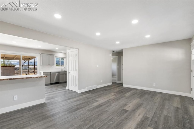 unfurnished living room featuring recessed lighting, dark wood-style floors, visible vents, a sink, and baseboards