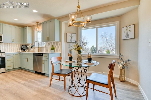 kitchen with green cabinets, a chandelier, light wood-style flooring, backsplash, and appliances with stainless steel finishes