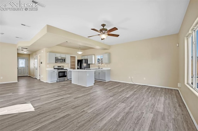 unfurnished living room featuring light wood-type flooring, baseboards, ceiling fan, and a healthy amount of sunlight