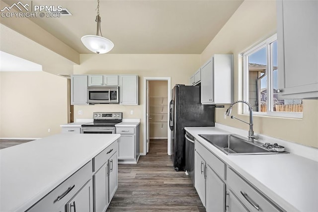 kitchen with a sink, hanging light fixtures, appliances with stainless steel finishes, light countertops, and dark wood-style flooring