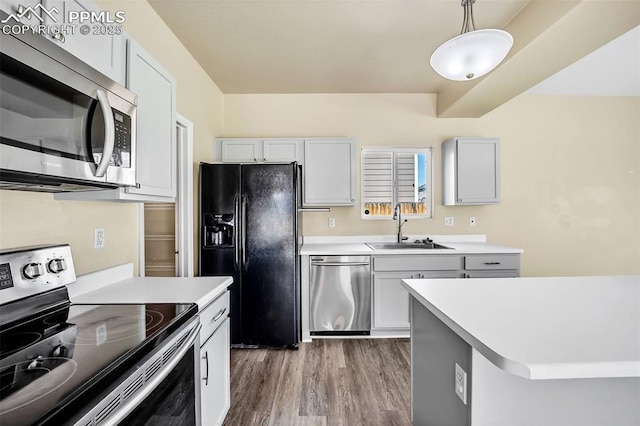 kitchen featuring wood finished floors, a sink, hanging light fixtures, light countertops, and appliances with stainless steel finishes