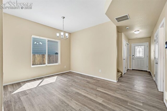 interior space featuring baseboards, wood finished floors, a chandelier, and visible vents