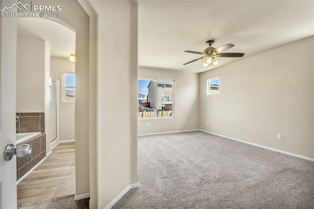 carpeted empty room featuring arched walkways, ceiling fan, a wealth of natural light, and baseboards