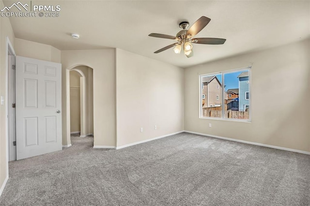 carpeted empty room featuring baseboards, arched walkways, and ceiling fan