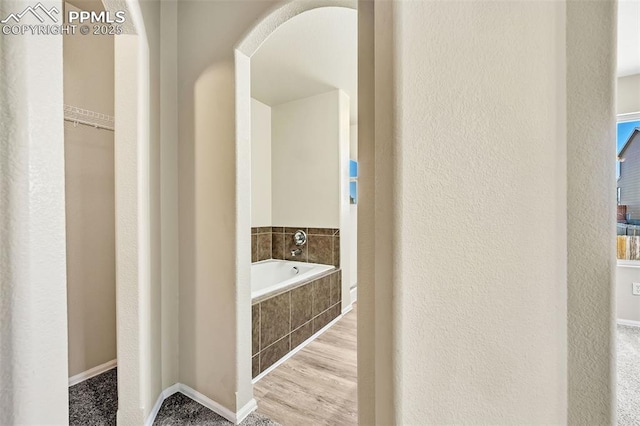 full bath featuring a walk in closet, a bath, and baseboards