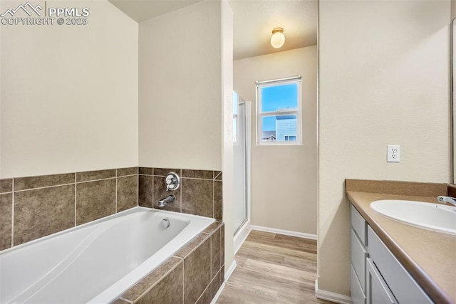 bathroom with a shower stall, wood finished floors, vanity, a bath, and baseboards