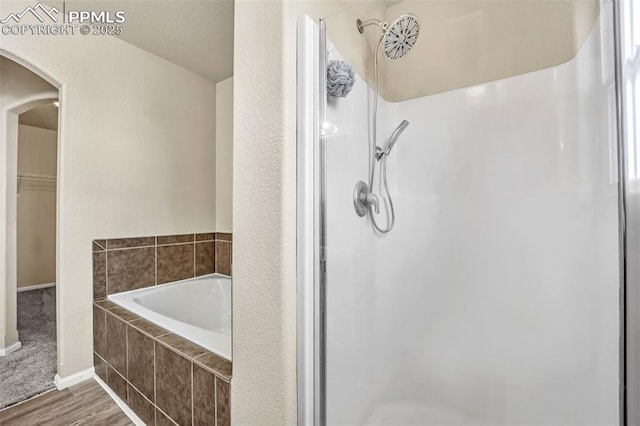 full bath with a walk in closet, a bath, a shower stall, and wood finished floors