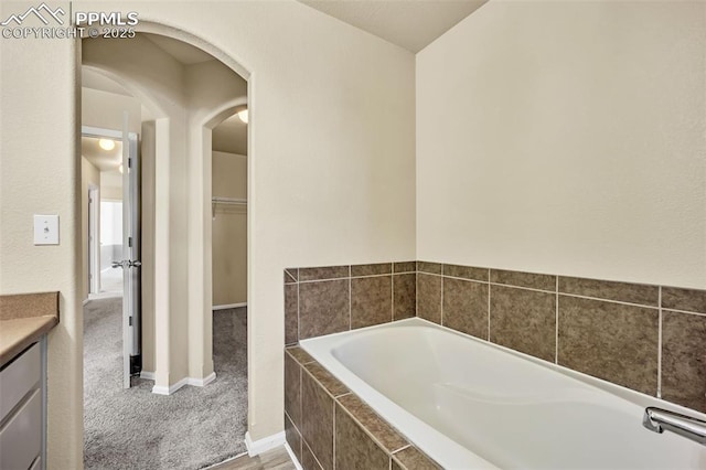 bathroom with a bath, baseboards, a walk in closet, and vanity