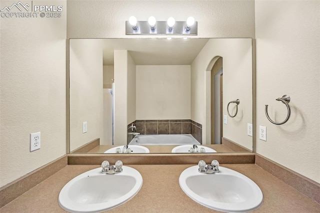 full bathroom with a textured wall, a garden tub, a sink, and double vanity