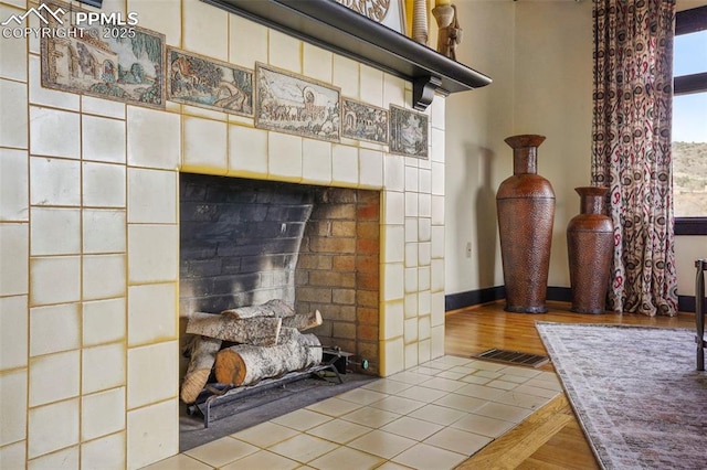details featuring a tiled fireplace, visible vents, baseboards, and wood finished floors