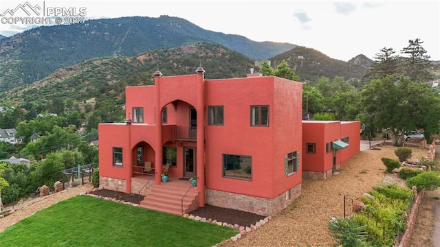 exterior space with a front yard, a mountain view, stucco siding, and a balcony