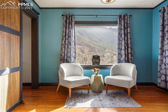 living area with wood finished floors, wooden walls, baseboards, and ornamental molding