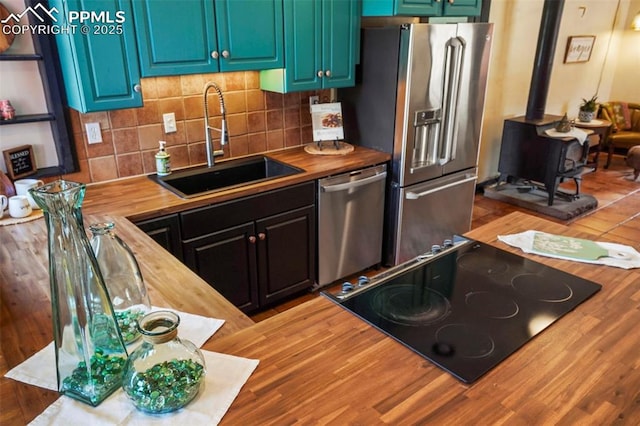 kitchen featuring a wood stove, tasteful backsplash, butcher block counters, a sink, and stainless steel appliances