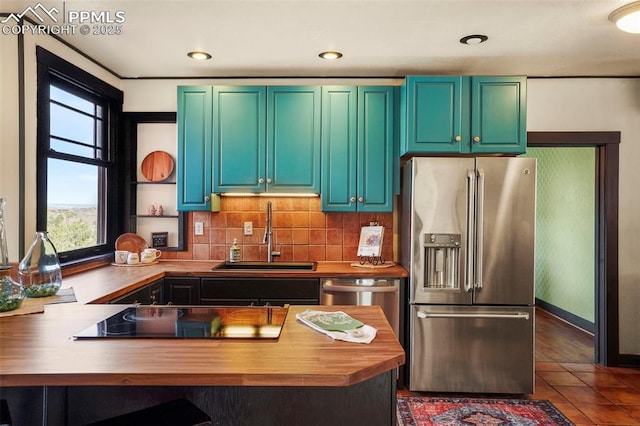 kitchen with tasteful backsplash, butcher block counters, a peninsula, a sink, and stainless steel appliances