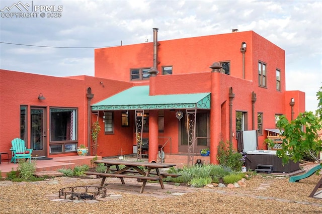 rear view of house featuring a patio area, an outdoor fire pit, stucco siding, and a hot tub