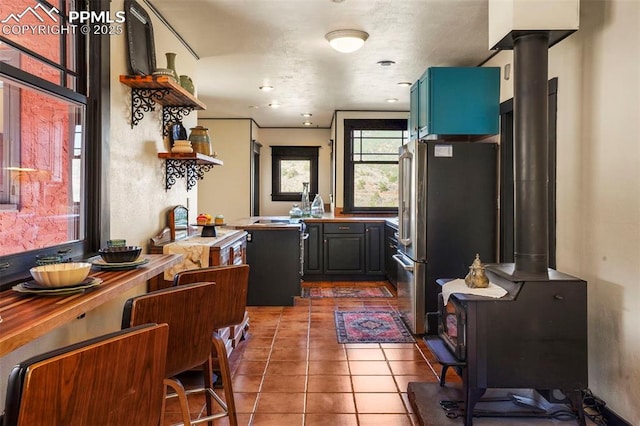 kitchen featuring tile patterned floors, freestanding refrigerator, open shelves, and a wood stove