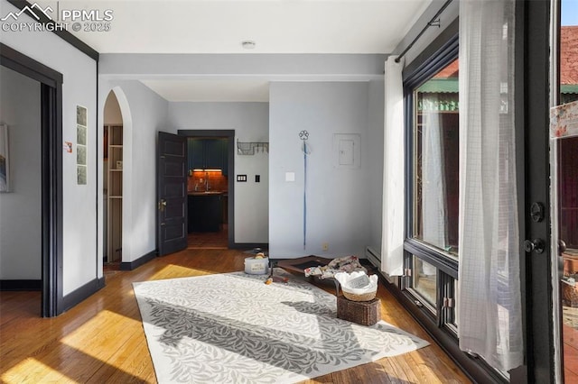 foyer entrance with arched walkways, wood finished floors, a baseboard heating unit, and baseboards