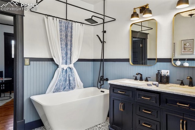 bathroom featuring a freestanding tub, double vanity, a sink, and a wainscoted wall