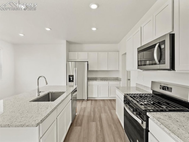 kitchen featuring light wood finished floors, stainless steel appliances, white cabinets, and a sink