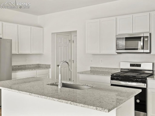 kitchen with a sink, an island with sink, white cabinetry, appliances with stainless steel finishes, and light stone countertops