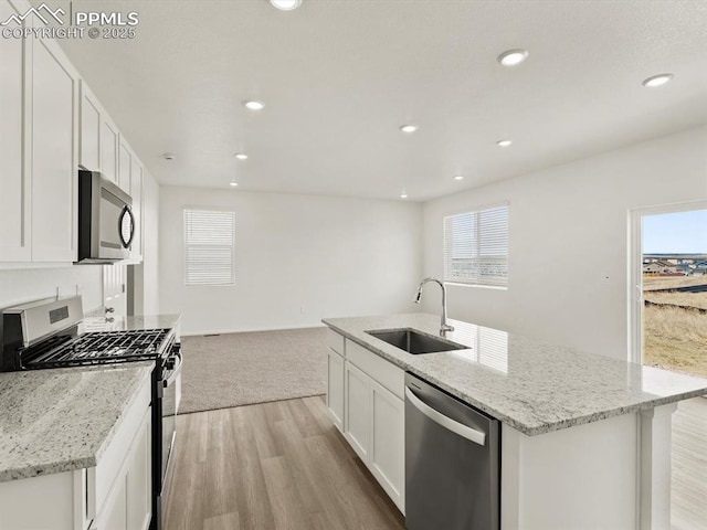 kitchen with a sink, a kitchen island with sink, stainless steel appliances, light wood-style flooring, and white cabinets