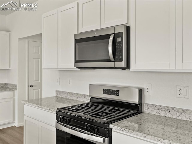 kitchen with wood finished floors, white cabinetry, light stone countertops, and stainless steel appliances