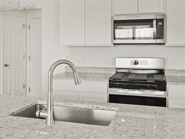 kitchen featuring light stone countertops, white cabinetry, stainless steel appliances, and a sink