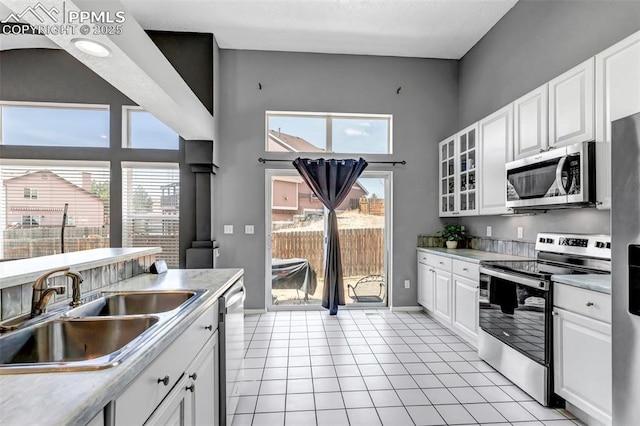4626 Hotspur Dr, Colorado Springs, CO 80922 - kitchen with stainless steel appliances, a sink, light tile patterned flooring, white cabinetry, and a high ceiling