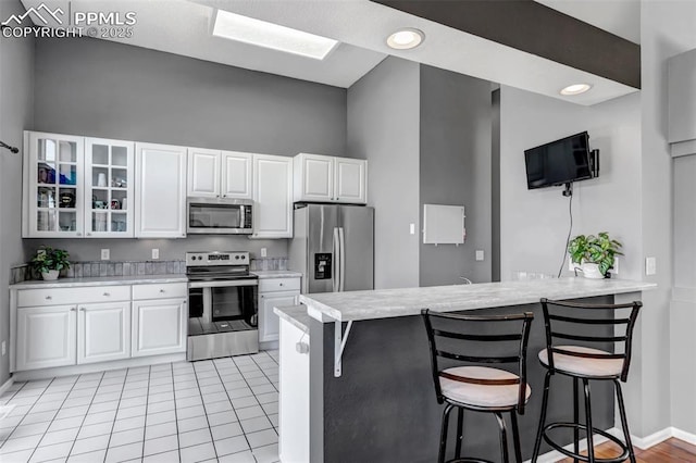 4626 Hotspur Dr, Colorado Springs, CO 80922 - kitchen with glass insert cabinets, light countertops, a kitchen bar, a peninsula, and appliances with stainless steel finishes