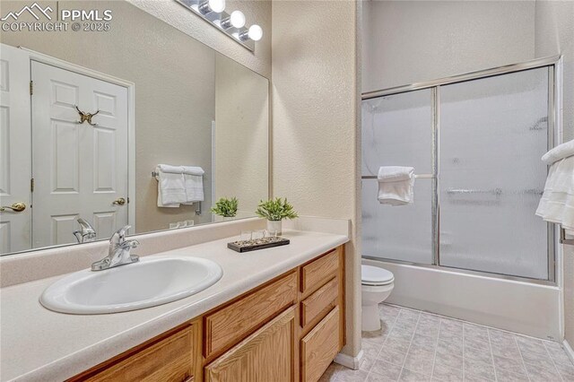 5542 Sunshade Pt, Colorado Springs, CO 80923 - bathroom featuring toilet, vanity, a textured wall, and bath / shower combo with glass door