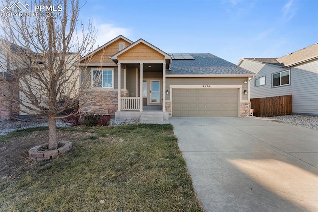 craftsman-style house featuring solar panels, driveway, stone siding, fence, and an attached garage