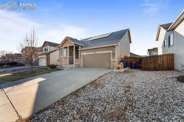 view of front of property with fence, concrete driveway, an attached garage, solar panels, and stone siding
