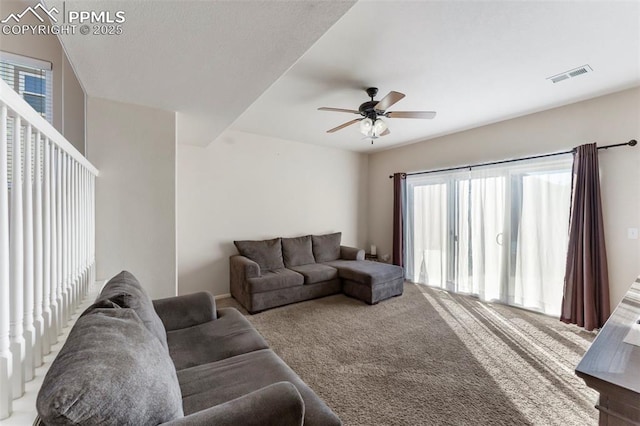 living room featuring plenty of natural light, a ceiling fan, visible vents, and carpet floors