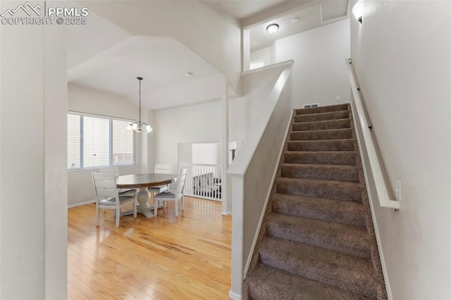 staircase featuring wood-type flooring, an inviting chandelier, visible vents, and baseboards
