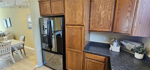kitchen featuring brown cabinetry, black fridge with ice dispenser, and baseboards