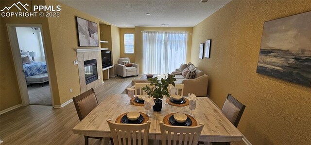 dining area featuring wood finished floors, a textured wall, baseboards, and a tile fireplace