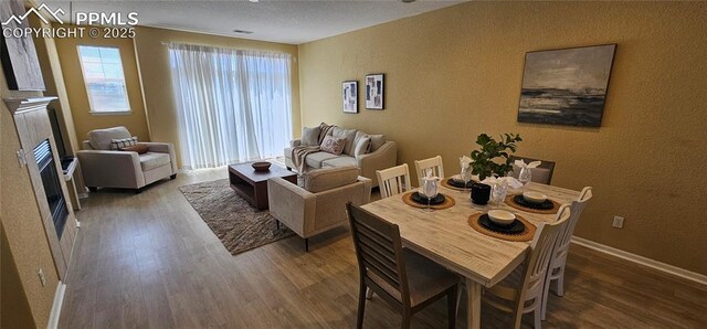 living room featuring wood finished floors, a textured wall, baseboards, and a fireplace