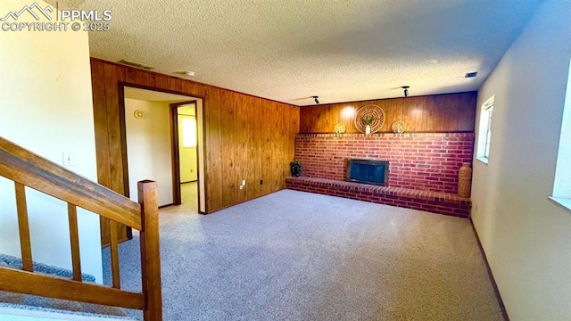 5125 Thistle Ct, Colorado Springs, CO 80917 - unfurnished living room featuring a brick fireplace, wood walls, carpet floors, a textured ceiling, and stairway