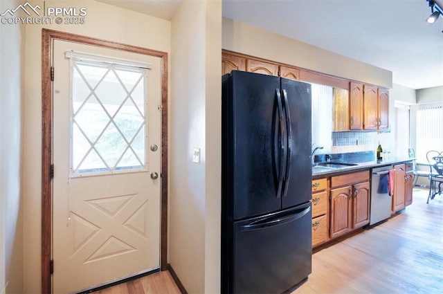 kitchen with stainless steel dishwasher, freestanding refrigerator, decorative backsplash, a sink, and light wood-style flooring