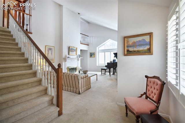 interior space with a glass covered fireplace, light carpet, baseboards, high vaulted ceiling, and stairway