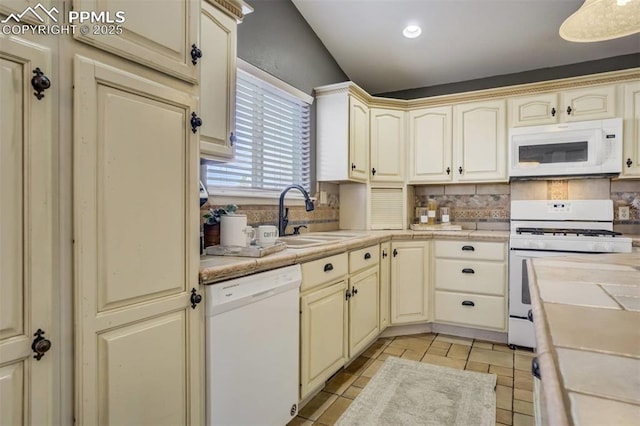 kitchen featuring cream cabinetry, a sink, and white appliances