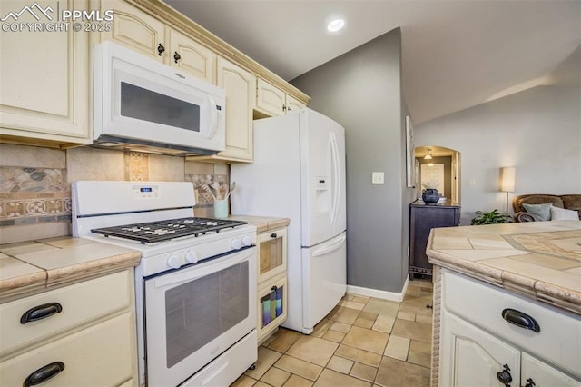 kitchen featuring cream cabinets, tasteful backsplash, tile counters, and white appliances