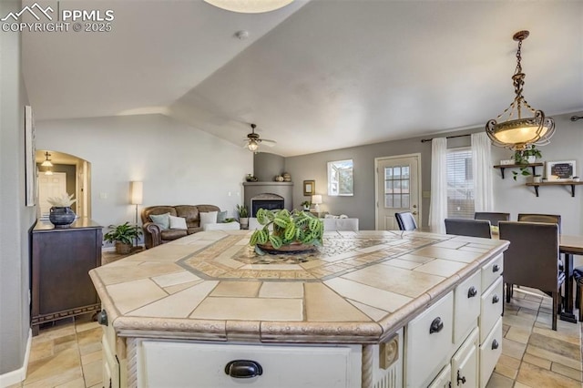 kitchen with white cabinets, vaulted ceiling, ceiling fan, a fireplace, and tile countertops