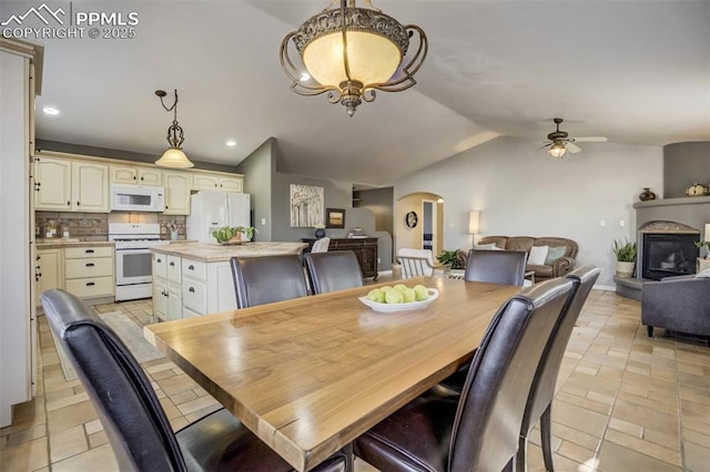 dining room with recessed lighting, vaulted ceiling, a ceiling fan, arched walkways, and a glass covered fireplace