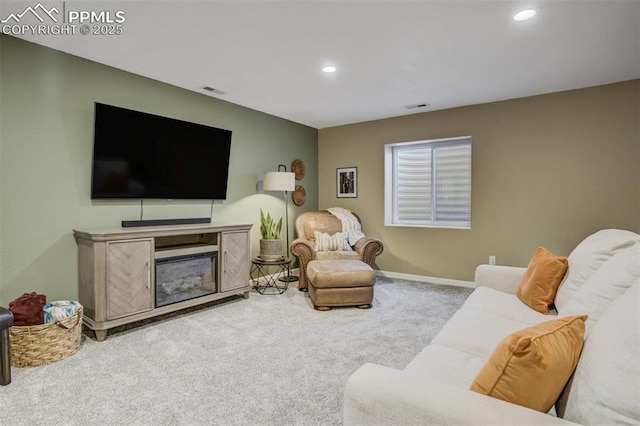 carpeted living room featuring baseboards, a glass covered fireplace, visible vents, and recessed lighting