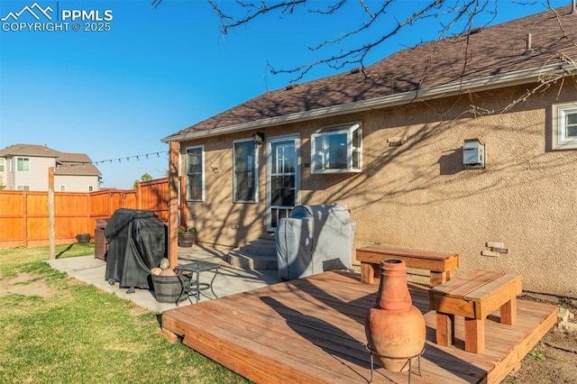 rear view of property featuring fence, a lawn, a shingled roof, and stucco siding