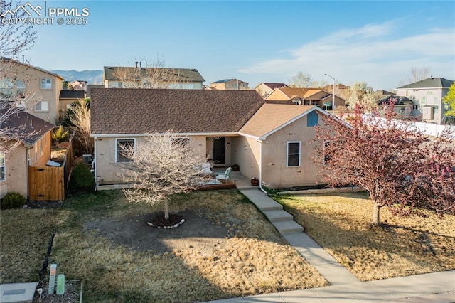 ranch-style house featuring stucco siding, fence, a residential view, and a front yard