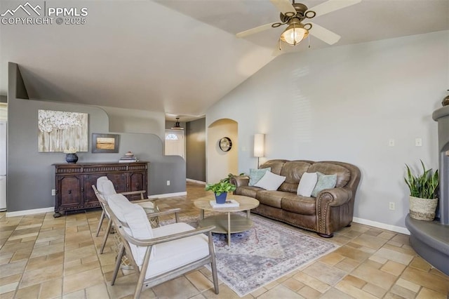living area with arched walkways, vaulted ceiling, baseboards, a ceiling fan, and stone finish flooring