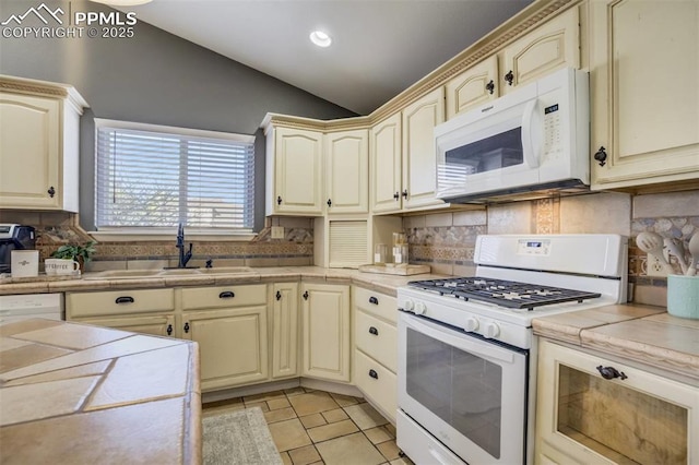 kitchen featuring lofted ceiling, white appliances, a sink, and cream cabinetry