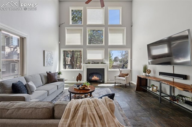 living area with ceiling fan, plenty of natural light, stone tile floors, and a towering ceiling